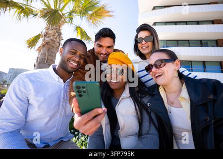 Verschiedene Freunde lachen, während sie Inhalte auf dem Smartphone im Freien ansehen Stockfoto