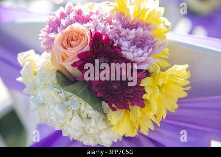 Eine lebhafte Hochzeitsstuhl-Dekoration mit einer Pfirsichrose, lila Chrysanthemen, gelben Dahlien und weißen Hortensien. Stockfoto
