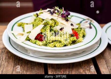 Köstliche Fusilli-Pasta mit grünem Pesto, Kirschtomaten und veganen Parmesanraspeln. Frisches pflanzliches italienisches Gericht, serviert in einem Restaurant Stockfoto