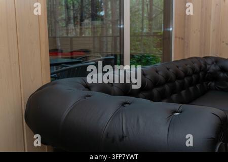 Schwarzes Chesterfield-Sofa aus Leder in einem Raum mit Panoramafenster Stockfoto