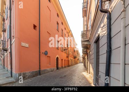 Cuneo, Italien - 27. Juli 2026: Bezaubernde historische Gasse mit traditionellen orangefarbenen und pastellfarbenen Fassaden, Kopfsteinpflaster und traditioneller Architektur Stockfoto