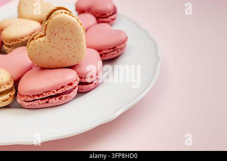 Vanille-Herz-Makrone ruht auf rosa Herz-Makronen auf einem weißen, muschelförmigen Teller, Nahaufnahme mit Kopierraum auf Rosa. Stockfoto