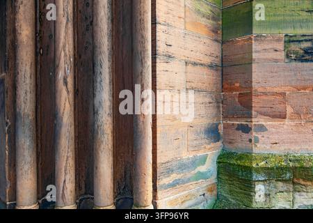 Nahaufnahme einer historischen verwitterten Sandsteinwand in Orange mit geschnitzten Säulen und grünem Moos auf dem Blockhintergrund Stockfoto