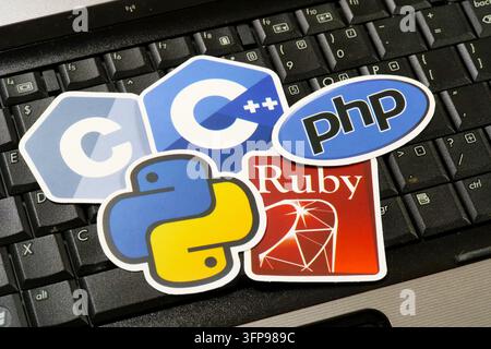 Nahaufnahme einer schwarzen Laptop-Tastatur, bedeckt mit fünf Programmierensprach-Aufklebern: das C-Logo auf einem grauen Sechseck, das C++-Logo auf einem blauen Sechseck Stockfoto