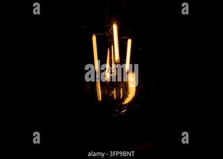 Glühen einer Vintage-LED-Filamentlampe in völliger Dunkelheit Stockfoto