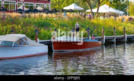 NISSWA, MN - 12. SEP 2024: Frau geht auf Steg an zwei klassischen Chris-Craft-Speedbooten vorbei bei einer Outdoor-Vintage-Bootschau mit Zelten und Gärten, Nisswa, Min Stockfoto