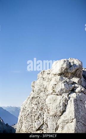 Eine Nahaufnahme zeigt eine schroffe Felsformation vor einem lebendigen blauen Himmel. In der Ferne sind Bergketten sichtbar, die ein Gefühl von Stockfoto