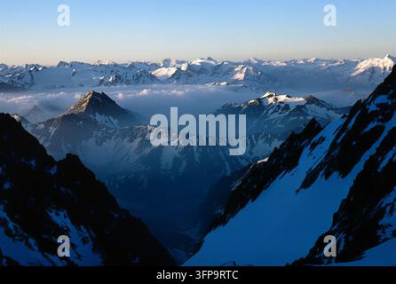 Ein atemberaubender Blick zeigt schneebedeckte Gipfel, die über einer dicken Wolkenschicht aufragen. Die Szene ist in das weiche, kühle Licht des frühen Morgens getaucht. Stockfoto