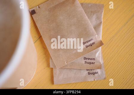 Braune Zuckerpäckchen, die auf einem Holztisch neben einer Tasse platziert sind Stockfoto