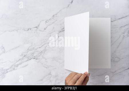 Oberblick-Sequenz von offen bis geschlossen, leeres weißes Grußkarten-Modell auf Marmorhintergrund mit Kopierraum: Hand öffnet eine leere weiße gefaltete Grußkarte Stockfoto