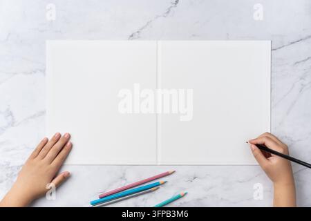 Top-Down-Sequenz von offen zu geschlossen, leerer weißer Grußkartenmockup auf Marmorhintergrund mit Platz für Text: Kinderhand schreibt mit Farbstift auf o Stockfoto