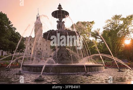 Parlament von Quebec City am Abend von Sonnenstrahlen zwischen Bäumen beleuchtet mit der Fontaine de Tourny im Vordergrund, Kanada Stockfoto