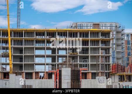 Ein mehrstöckiges Wohnhaus, das im Betonrahmen- und Gerüstbau mit großen Turmdrehkränen unter einem blauen Himmel steht Stockfoto