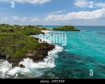 Felsige Küste mit brechenden Wellen, die auf klares, türkisfarbenes Wasser an der üppigen Inselküste von Malapascua, Philippinen, treffen Stockfoto