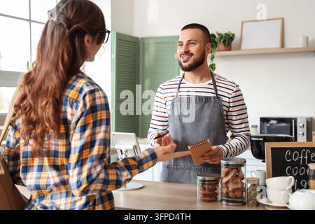 Kundenservice und Kleinunternehmen, Barista nimmt eine Bestellung von einem Kunden in einem Café mit Kassensystem und Gebäckauslage entgegen Stockfoto