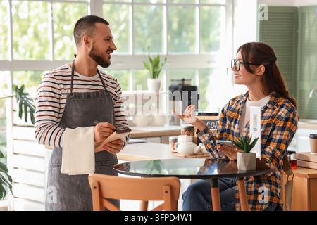 Kundenservice und Gastgewerbe, Kellner nimmt die Bestellung einer Kundin in einem modernen Café mit digitaler Speisekarte und Mobilzahltechnik auf Stockfoto