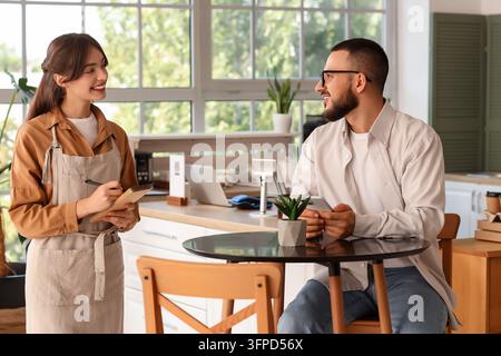 Kundenservice und Gastfreundschaft, Kellnerin nimmt Bestellung von einem männlichen Gast in einem modernen Café mit freundlicher Interaktion und kleiner Geschäftsatmosphäre auf Stockfoto