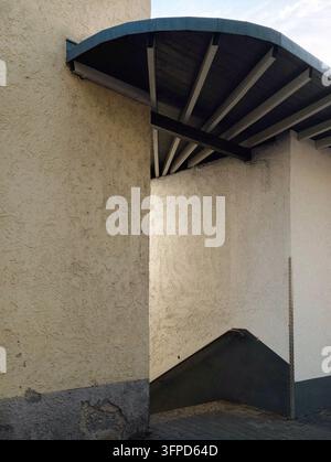 Niedrigwinkelaufnahme von verwitterter Stuckarchitektur mit gewölbtem Dach, tief im Schatten liegenden Balken, hellen Wänden und schmalem Eingang darunter, wodurch starke Linien und Textur entstehen Stockfoto