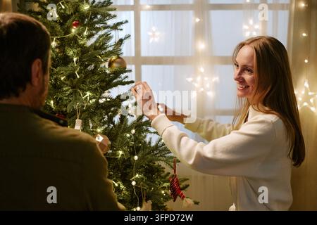 Glückliches Paar dekoriert zusammen den Weihnachtsbaum zu Hause Stockfoto