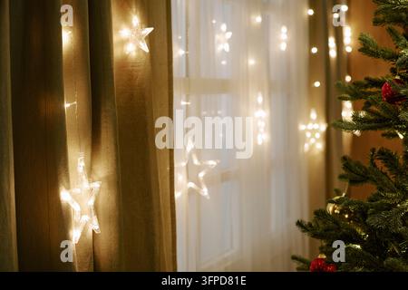 Leuchtende Sternen-Lichterketten und Weihnachtsbaum im Wohnraum Stockfoto