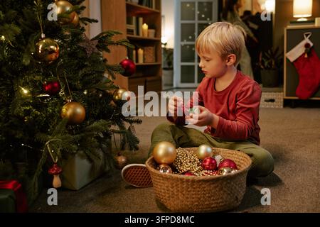 Junge dekoriert zu Hause den Weihnachtsbaum mit Kugeln für die Feiertage Stockfoto