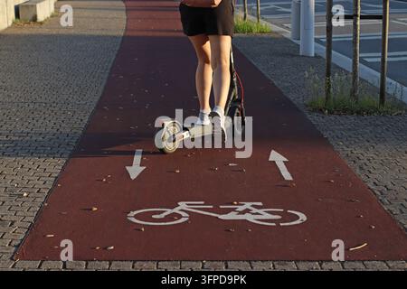 Elektro-Scooter fährt auf einem speziellen Radweg, der mit Fahrradsymbolen und Richtungspfeilen markiert ist, urbane Mikromobilität, Verkehrssicherheit, geteilt Stockfoto