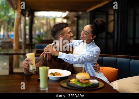 Ein vielseitiges Paar mit Feinschmecker genießt ein zwangloses Abendessen und einen Telefonmoment, bei dem sonnige Vibes und Drinks geteilt werden Stockfoto