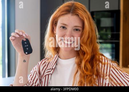 Junge rothaarige Frau lächelt und hält Autoschlüssel in einer modernen Hausküche, nachdem sie ein Auto gekauft hat Stockfoto