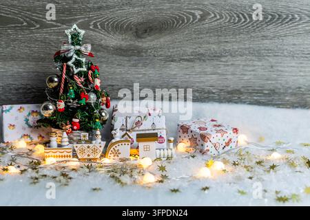 Dekorierter Miniatur-Weihnachtsbaum, der in künstlichem Schnee mit Geschenkkartons, einer Spielzeugbahn und Lichterketten steht Stockfoto