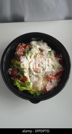 Meeresfrüchte-Caesar-Salat in einer schwarzen Takeaway-Schüssel, frische Garnelen und Calamari mit knackigem Salat, Tomaten und Parmesan Stockfoto
