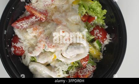 Meeresfrüchtes-Caesar-Salat mit Garnelen, Calamari, Muscheln, frischem Salat, Kirschtomaten und Parmesan in einer Lieferbox Stockfoto