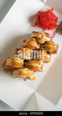 Gebratene Sushi-Rollen mit scharfer Soße und Wasabi-Mayonnaise in einer Take-away-Box, bereit für die Lieferung oder eine schnelle Mahlzeit Stockfoto
