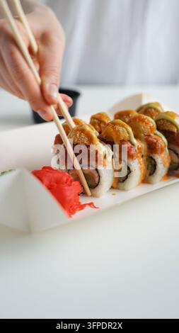 Hand nimmt Tempura-Sushi-Rollen mit Stäbchen, genießt japanische Küche und Takeout-Essen Stockfoto