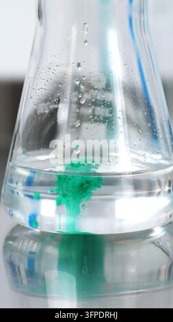 Erlenmeyerkolben, der grünen Farbstoff zeigt, der sich in klarer Flüssigkeit ausbreitet, bei einem wissenschaftlichen Chemieexperiment Stockfoto
