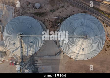 Luftaufnahme von zwei großen metallischen Getreidesilos, die durch eine Stege verbunden sind, in der Nähe eines Bahngleises in Eaton, Colorado, Vereinigte Staaten. Stockfoto