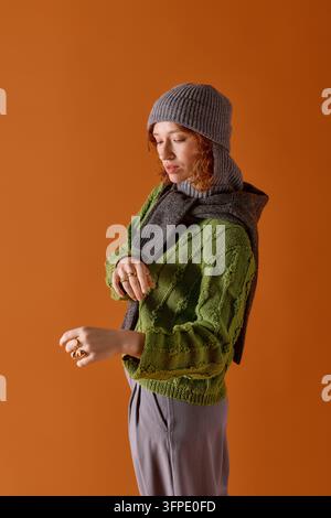 Eine junge Frau mit lockigen Haaren trägt einen kuscheligen Pullover und einen Winterhut und umarmt den Winterstil. Stockfoto