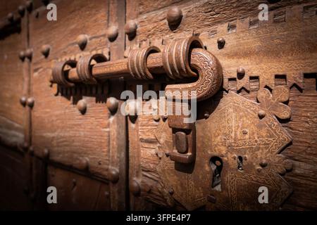 Ein langer schmiedeeiserner Riegel mit dekorativen Details schließt eine alte, genagelte Holztür mit Scharnier, Gubbio, Umbrien, Italien Stockfoto