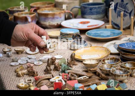 Handgefertigte Keramikgegenstände, die auf einem Flohmarkt im Freien ausgestellt sind, darunter Tassen, glasierte Schalen, Tierfiguren, Miniaturboote und dekorative Geschirrstücke. Stockfoto