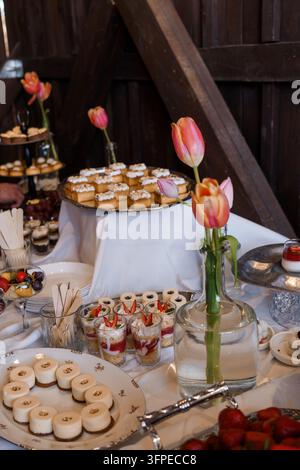 Elegante Dessertauswahl in einer holzverkleideten Halle, die eine warme Landhaus-Stimmung für Hochzeitsveranstaltungen schafft Stockfoto