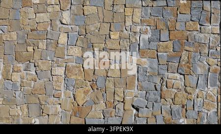 Große Stützmauer mit flachen Steinen in braun, grau und gelb. Ganzes Bild, Hintergrund und Textur. Stockfoto