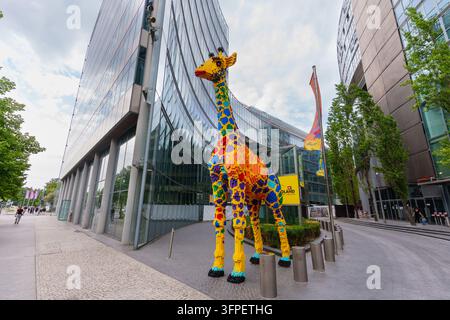 Berlin, Deutschland – 28. August 2026: Vollständige Ansicht einer massiven Giraffenstatue aus Spielzeugbausteinen, die auf dem Gehweg vor zeitgenössischen Glasgebäuden am Pots steht Stockfoto