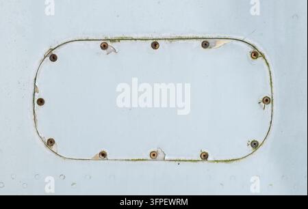 Nahaufnahme einer verwitterten weiß gestrichenen Metallplatte mit einer abgerundeten rechteckigen Lukenform, die durch rostige Kreuzschrauben befestigt ist Stockfoto