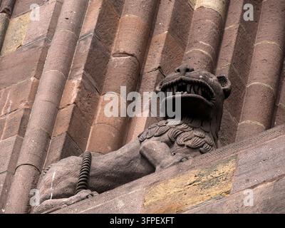 Detaillierte Sandstein-Löwenskulptur, die auf der Außenseite der romanischen Wormser Domkirche in Deutschland thront und eine kunstvoll geschnitzte Mähne und ein geöffnetes Maul zeigt. Stockfoto