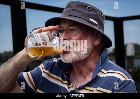 Nahaufnahme eines bärtigen älteren Mannes mit Hut, der ein Glas Bier in Dordrecht genießt Stockfoto