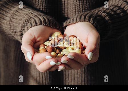 Frau hält eine Handvoll gemischter Nüsse in beiden Händen. Gesunder Snack-Hintergrund für natürliche Lebensmittel, Pflanzenproteine, Ernährung und ausgewogene Ernährung. Stockfoto