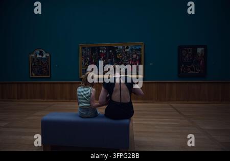 Mutter und Tochter teilen einen Moment auf einer Galeribank mit Blick auf Renaissance-Religionsgemälde im Kunstmuseum Stockfoto