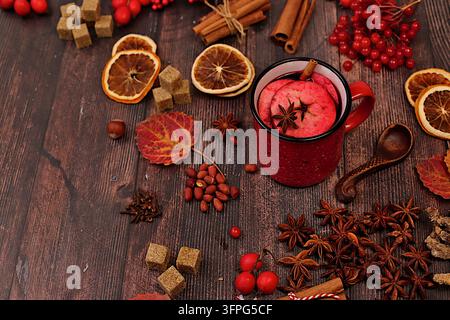 Heißer Glühwein in einem Eisenbecher mit Gewürzen, gebranntem Zucker, Nelken, Nüssen, Zimt, Sternanis, Ebereschenbeeren und Hagebutten, abstrakte Herbststillleben c Stockfoto