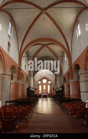Historisches Kircheninnere in Mailand, Italien, mit roten Ziegelrippengewölben, massiven Steinsäulen, religiösen Fresken, Holzbankreihen und einem verzierten Altar Stockfoto