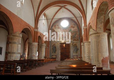 Historisches Kircheninnere in Mailand, Italien, mit roten Ziegelrippengewölben, massiven Steinsäulen, religiösen Fresken, Holzbankreihen und einem verzierten Altar Stockfoto