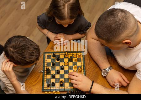 Hohe Blickwinkelansicht von Onkel, Neffe und Nichte, die sich auf ein Schachspiel konzentrieren. Stockfoto
